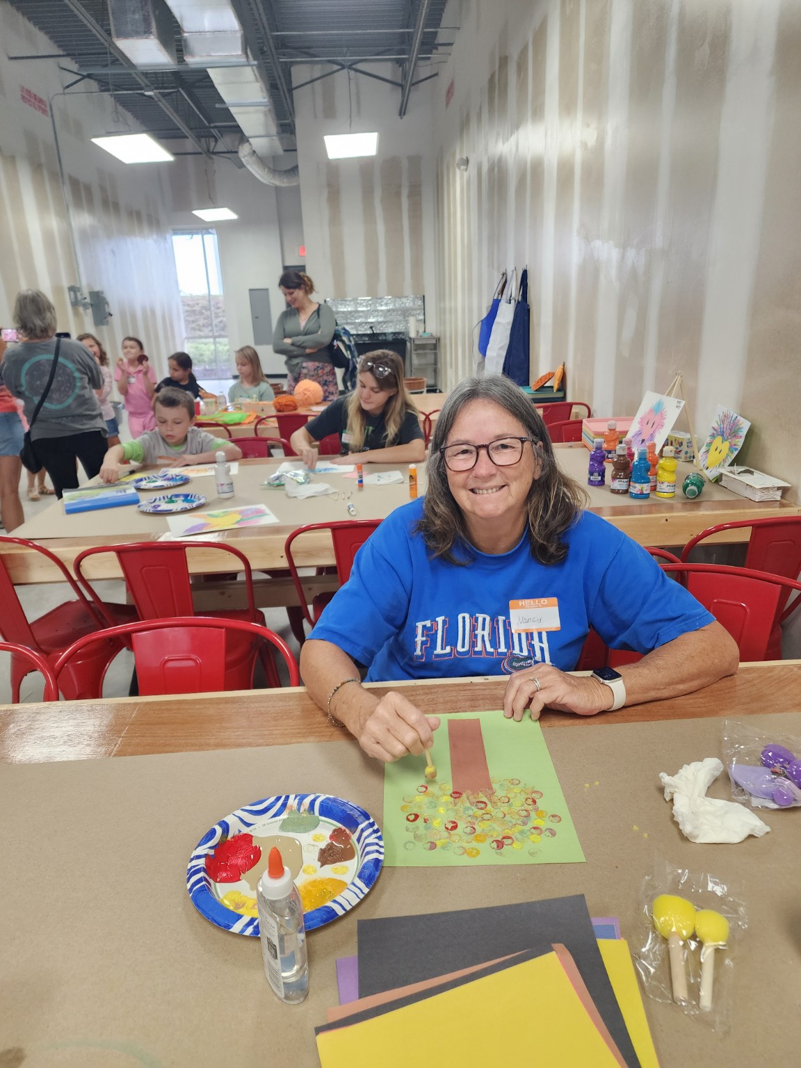 A smiling guest painting an autumn tree while families craft behind her