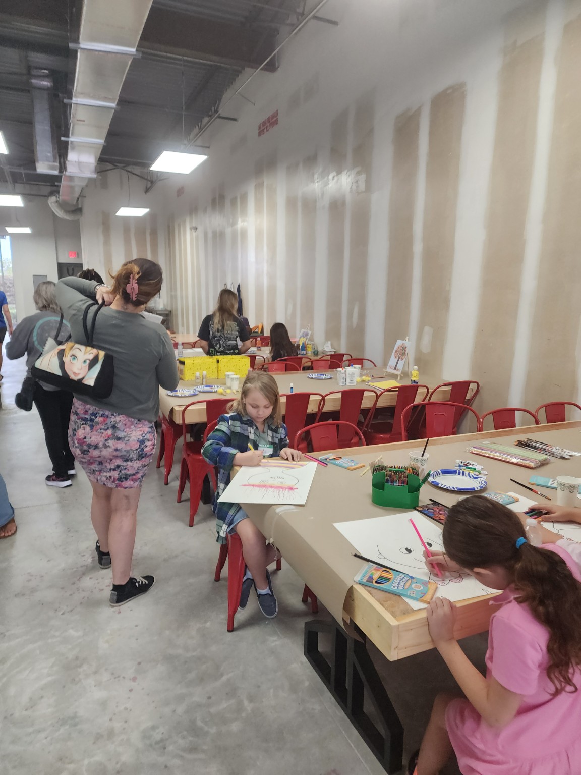 Children working at a long craft table while adults visit nearby