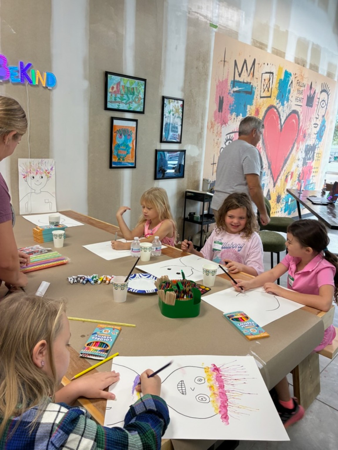 Children painting colorful portraits together near the studio heart mural