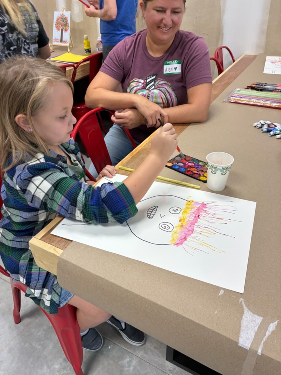 A child painting a colorful portrait while a smiling adult watches