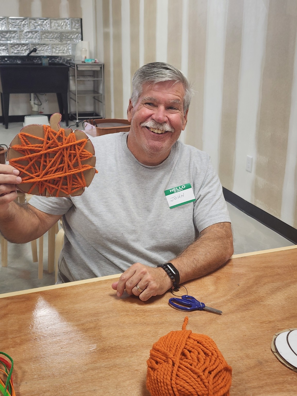 A smiling guest holding up an orange yarn-wrapped pumpkin craft