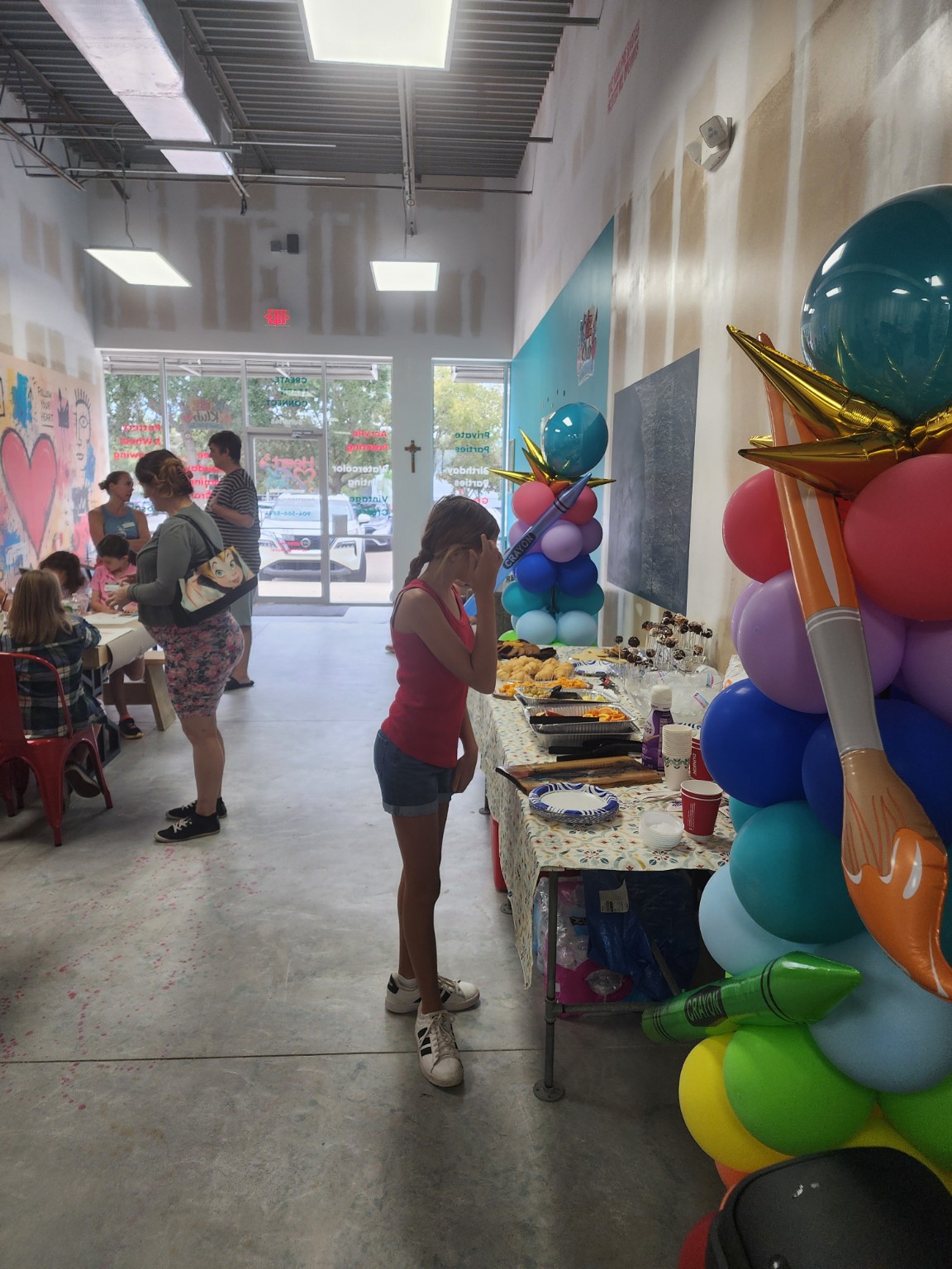Guests enjoying refreshments beside colorful balloon columns and a giant paintbrush decoration