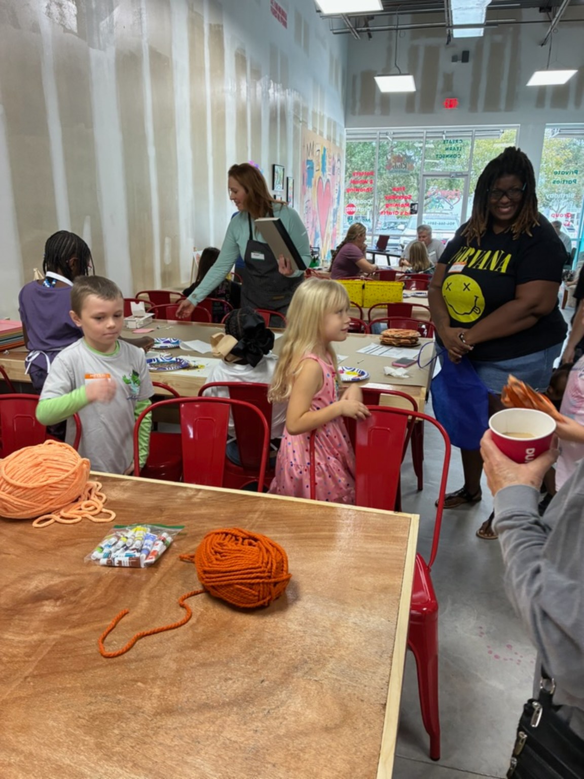 Children and adults enjoying opening day around craft tables with yarn and art supplies
